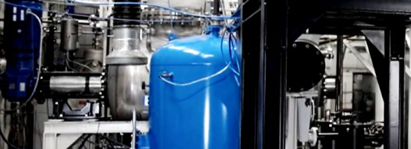 Industrial machinery with a large blue tank, metal pipes, and wires in a factory-like setting.