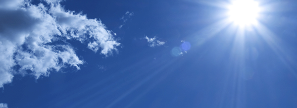 Bright sun shining in a clear blue sky with a few white clouds and visible sun rays.