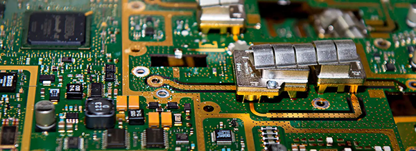 Close-up of a green and gold circuit board with electronic components, chips, and metal parts visible.